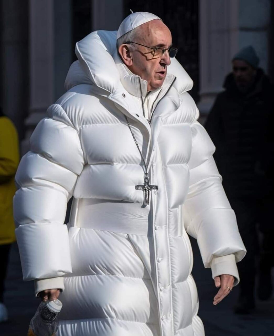 Pope Francis walking outdoors in a long white quilted puffer coat, with a crucifix on a chain around his neck.